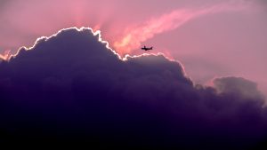 plane flying into dark clouds during a colorful sunset
