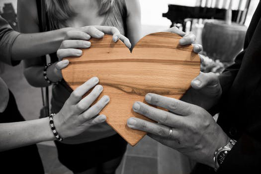 black and white photo of hands holding a wooden heart, which is in color