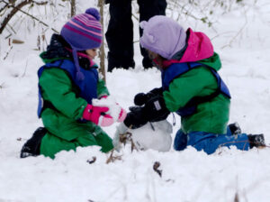 Photo of two kids making a snowman in the snow