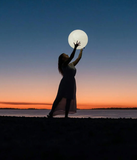 woman at sunset holding up the moon